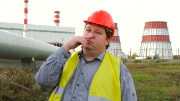 発電所の前で彼の鼻を選ぶカメラを直接見ている労働者、エンジニア、電気技師 — ストック動画