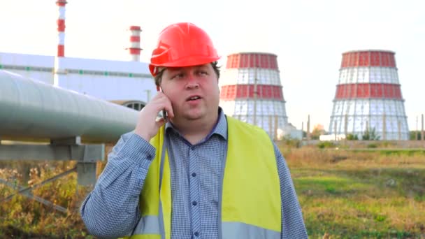 İşçi, mühendis ya da elektrikçi doğrudan kameraya bakıyor ve bir elektrik santralinin önünde telefonla konuşuyor. — Stok video