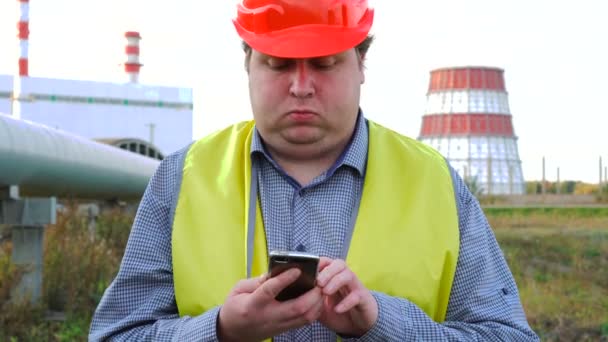 Trabalhador, engenheiro ou eletricista olhando diretamente para a câmera usando o smartphone na frente de uma central elétrica — Vídeo de Stock
