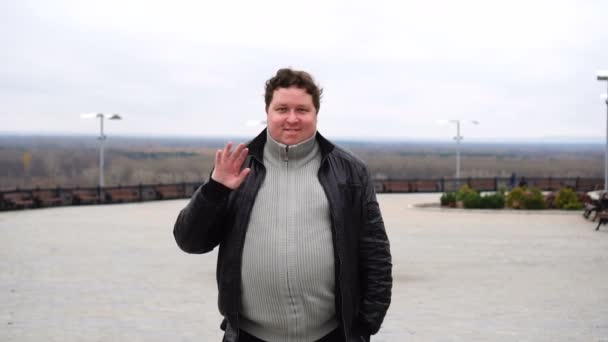 Zoom en el retrato de hombre gordo feliz mirando a la cámara y saludando por las olas de su mano — Vídeos de Stock