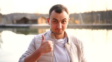 Genç yakışıklı bir adamın portresi. Beyaz sonbahar kıyafeti giyen bir adam kameraya bakar ve başparmağını kaldırır.
