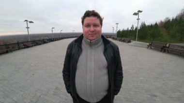 Geniş açı mercek: genç şişman adam şehir manzarasında duruyor ve kameraya özgüvenle bakıyor