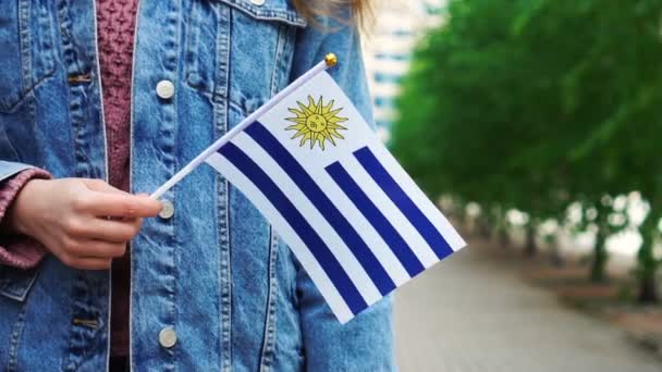 Cámara lenta: Mujer irreconocible con bandera uruguaya. Chica caminando calle abajo con bandera nacional de Uruguay — Vídeos de Stock