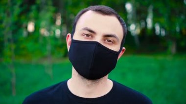 Bulutlu bir günde tepede siyah tıbbi maskeli genç bir adam. Yetişkin erkek kırsalda tek başına yürüyor.