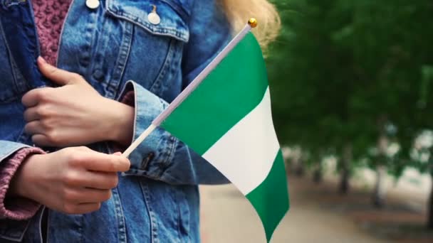 Zeitlupe: Unerkennbare Frau mit nigerianischer Flagge. Mädchen läuft mit nigerianischer Nationalflagge die Straße entlang — Stockvideo