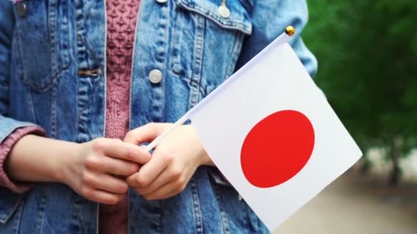 Cámara lenta: Mujer irreconocible sosteniendo bandera japonesa. Chica caminando por la calle con la bandera nacional de Japón — Vídeos de Stock