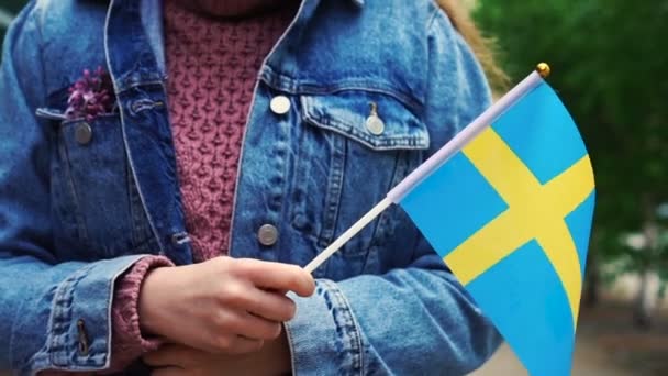 Slow motion: Oigenkännlig kvinna med svensk flagga. Flicka går nerför gatan med Sveriges flagga — Stockvideo