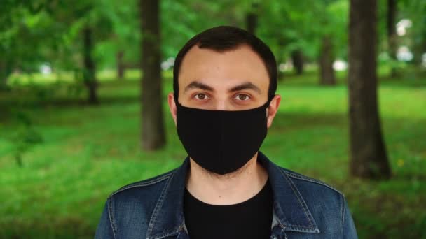 Joven guapo parado al aire libre usando máscara negra para proteger a otros de la propagación del virus — Vídeos de Stock