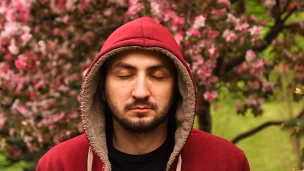 Schöner bärtiger Mann mit geschlossenen Augen meditiert am Frühlingstag gegen einen blühenden rosa Baum — Stockvideo