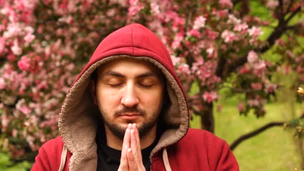 Yonng ember tartja a tenyerét, és gyakorolja a meditációt a tavaszi kertben a virágzó rózsaszín fa ellen — Stock videók