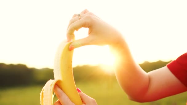 Femme épluchant et mordant la banane. Banane yammy mûre dans les mains féminines sur fond de coucher de soleil — Video