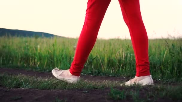 Жіночі ноги в червоних штанях крокують по ґрунтовій дорозі в полі, повільний рух — стокове відео