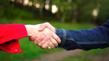 Yazın parkta yeşil çimen ve ağaçlardan oluşan bir arka planda iki genç insanın el sıkışması..