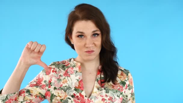 Rozzlobená mladá Evropanka nešťastná. Hezká dívka ukazující palec dolů znamení přes modré pozadí. — Stock video