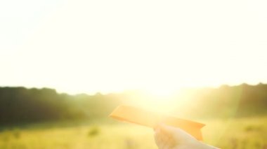 Turuncu gün batımında elinde kağıt uçak tutan bir kadın. Özgürlük kavramı