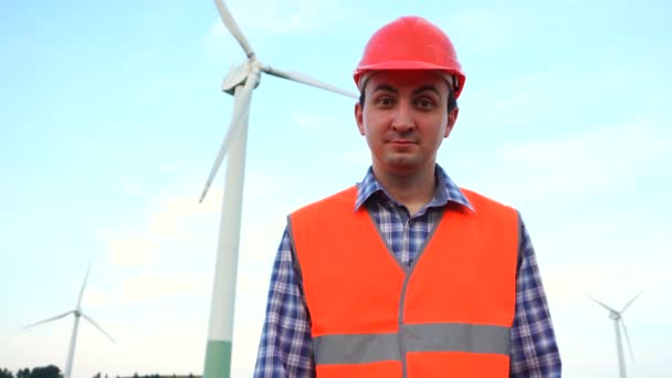 Ingenieur van de windturbinecentrale kijkt naar de camera. Windmolenpark en arbeider — Stockvideo