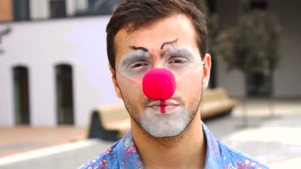 Jóképű férfi bohóc smink és piros orr néz kamera szabadban — Stock videók