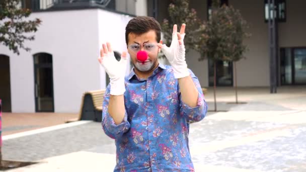 Молодой клоун с красным носом показывает пантомиму на улице — стоковое видео