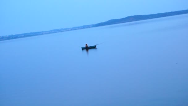 Fisherman swimming on inflatable rafting rubber boat on lake water surface at morning. — Stock Video