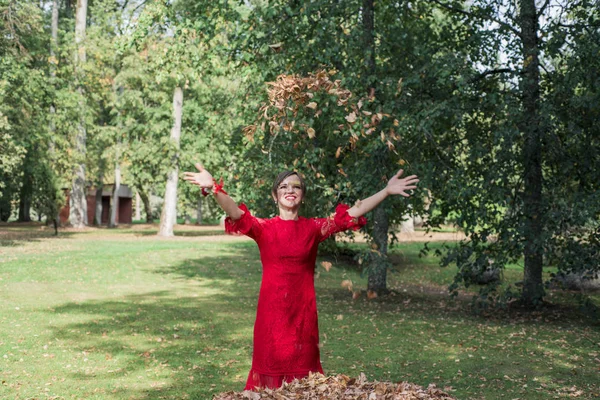 Young woman in red dress. Toss the autumn leaves upward. Abstract photo of happiness. Sunny Autumn day.