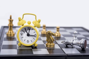 Beyaz arka plan üzerinde izole satranç tahtası. Küçük sarı alarm saati ile altın ve gümüş resimler.