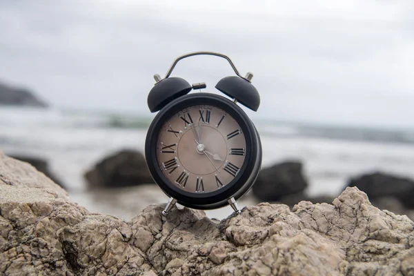 Reloj despertador en una roca al amanecer junto al océano —  Fotos de Stock