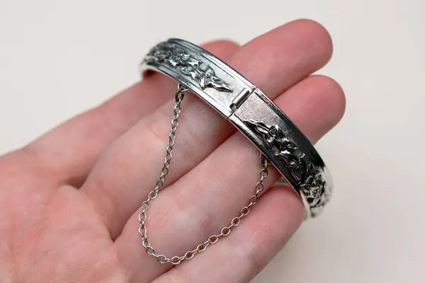 Silver bracelet with a chain in the hand on a white background.