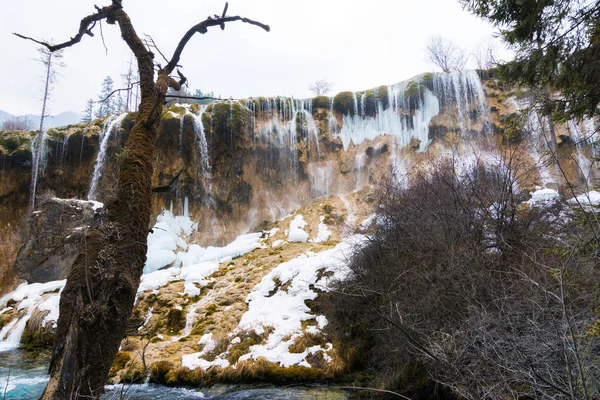 Waterfall in the forest. Stream of water on the rocks. Clean and cold water over the coniferous forest. Stones in the snow. Powerful rocks and a stream of water