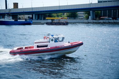 Nehir kıyısında mavi gökyüzünün altında şehir binaları arasında bir güvertesi olan bir eğlence teknesi.