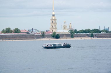 Nehir kıyısında mavi gökyüzünün altında şehir binaları arasında bir güvertesi olan bir eğlence teknesi.