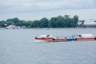 Nehir kıyısında mavi gökyüzünün altında şehir binaları arasında bir güvertesi olan bir eğlence teknesi.