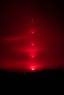 Geceleri kırmızı ışıkları olan uzun bir radyo direği bulutları kırmızı ışıkta yıkıyor. TV direği, şanzıman.