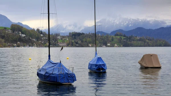 Boats covered with tarpaulin on lake Lucerne on a cloudy spring day. Town of Luzern, Switzerland.