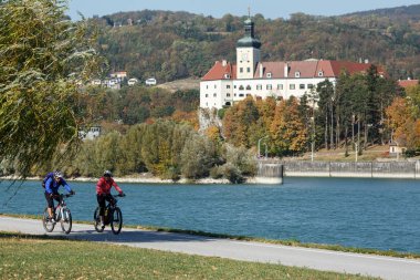 Ybbs An Der Donau / Austria - 14 Ekim 2018. Orta yaşlı çift sürme Tuna Nehri ünlü Bisiklete binme rotasında Donauradweg bisikletler. Persenbeug kale manzarası. Aşağı Avusturya, Europe.