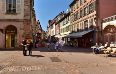Geleneksel ortaçağ evleri ile eski cadde boyunca yürüyen insanlar. Colmar, Fransa.