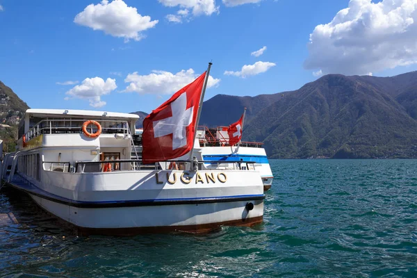 Lugano, SWitzerland - 17 Nisan 2018. Bahar güneşli bir günde Lugano Gölü. İsviçre bayrağıyla süslenmiş bir yolcu gemisinin görüntüsü. Lugano, Ticino kantonu, İsviçre, Avrupa.