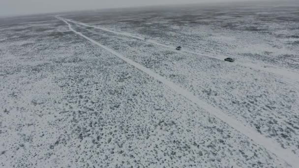 Vista aérea de suvs se movendo através do deserto coberto de neve no inverno. Cazaquistão Ocidental, Península de Mangyshlak . — Vídeo de Stock