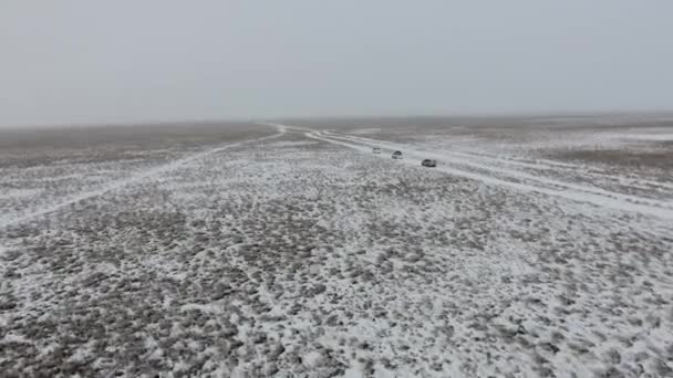 Vista aérea de suvs se movendo através do deserto coberto de neve no inverno. Cazaquistão Ocidental, Península de Mangyshlak . — Vídeo de Stock