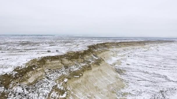 Два позашляховиків, рухаючись уздовж краю піщаних обриву засніженому пустелі в зимовий період. Західних областей Казахстану, Мангишлак. — стокове відео