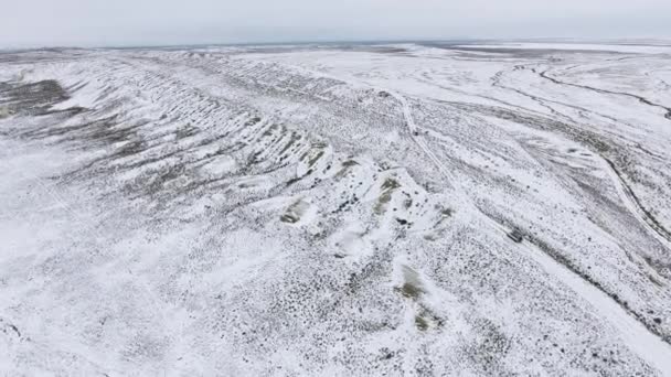 Три внедорожника движутся по краю песчаной скалы заснеженной пустыни зимой. Западный Казахстан, Мангышлакский полуостров . — стоковое видео