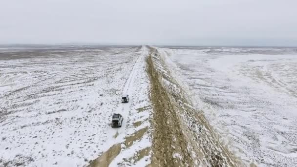 Drei Geländewagen bewegen sich im Winter am Rand einer sandigen Klippe der schneebedeckten Wüste entlang. Westkasachstan, Halbinsel Mangyshlak. — Stockvideo