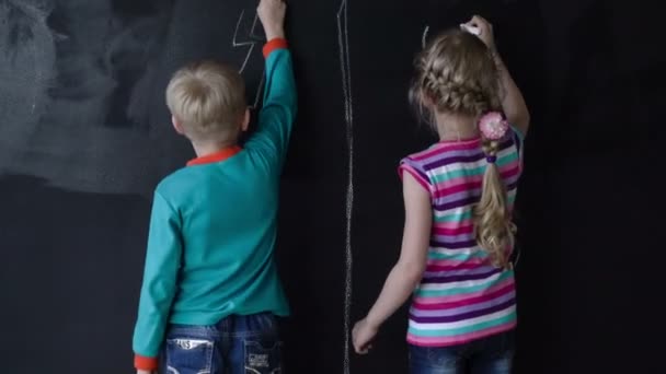 Mooi wit meisje en jongen tekenen met een krijt op een zwarte muur. Timelapse. — Stockvideo