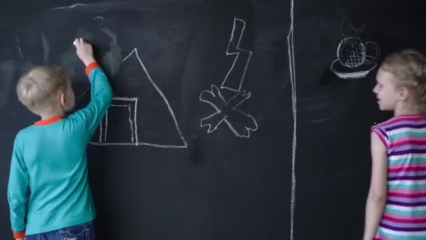 Mooi wit meisje en jongen tekenen met een krijt op een zwarte muur. Timelapse. — Stockvideo