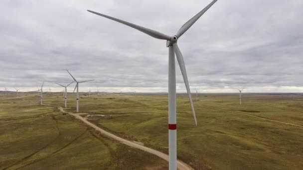 Movimiento de las palas de un gran aerogenerador en un campo sobre un fondo de naranja puesta de sol en el horizonte con una hermosa colinas. Fuentes de energía alternativas. Parque de viento. Energía ecológica.Industrial — Vídeos de Stock