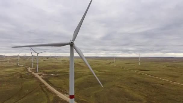 Movimiento de las palas de un gran aerogenerador en un campo sobre un fondo de naranja puesta de sol en el horizonte con una hermosa colinas. Fuentes de energía alternativas. Parque de viento. Energía ecológica.Industrial — Vídeo de stock