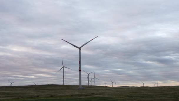 Motion the blades of a large wind turbine in a field against a background of orange sunset on the horizon with a beautiful hills. Alternative energy sources. Windy park. Ecological energy.Industrial — Stock Video