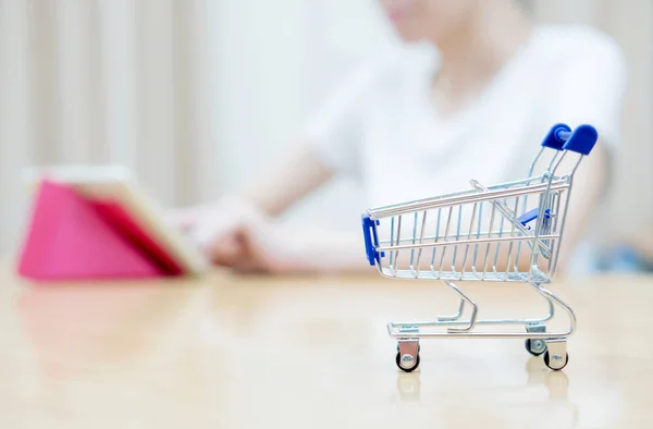 Frau kauft mit Miniatur-Einkaufswagen am Schreibtisch ein — Stockfoto