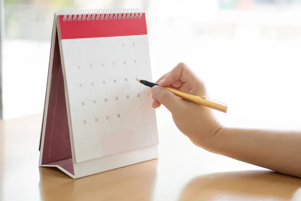 Woman hand carrying calendar and pointing on it by pen