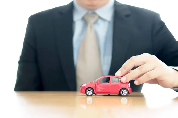 Empresario junto a un escritorio sosteniendo un coche de juguete . —  Fotos de Stock