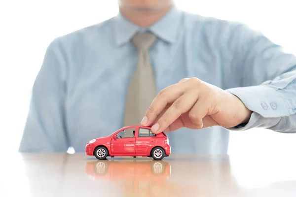 Empresario junto a un escritorio sosteniendo un coche de juguete . —  Fotos de Stock